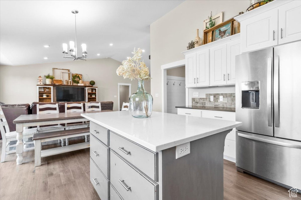 Kitchen with stainless steel refrigerator with ice dispenser, a center island, wood finished floors, white cabinetry, and lofted ceiling