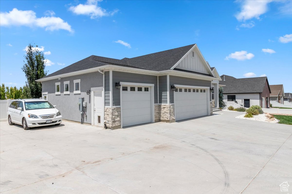 View of home's exterior with driveway, stone siding, an attached garage, and board and batten siding