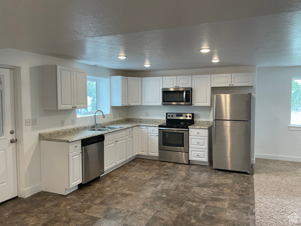 Kitchen featuring stainless steel appliances, white cabinets, a textured ceiling, and light stone counters