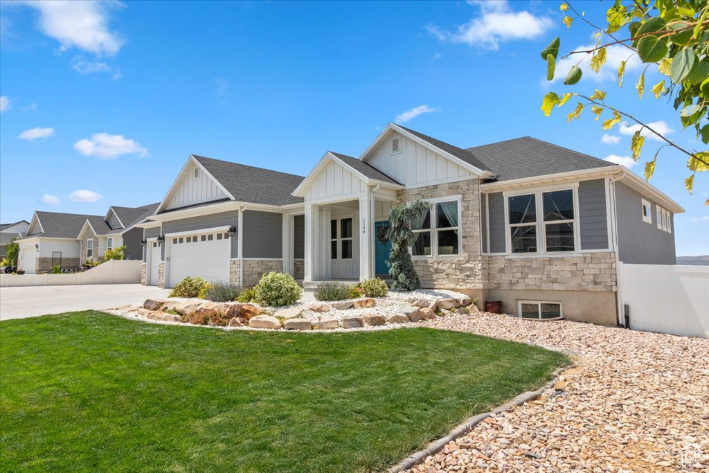 View of front facade featuring stone siding, board and batten siding, driveway, and a garage