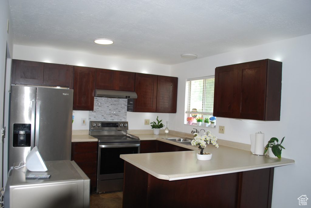 Kitchen with appliances with stainless steel finishes, a peninsula, light countertops, range hood, and dark brown cabinetry