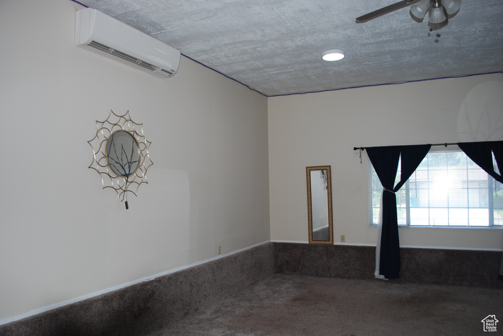Carpeted spare room featuring a wall mounted AC and a ceiling fan