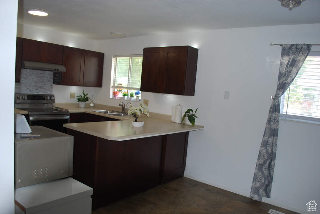 Kitchen with stainless steel electric range, a peninsula, under cabinet range hood, light countertops, and dark brown cabinets