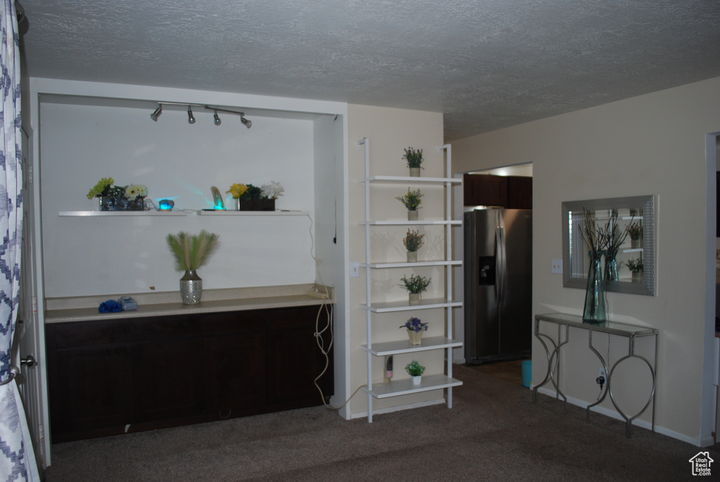 Carpeted bedroom featuring stainless steel fridge with ice dispenser and a textured ceiling