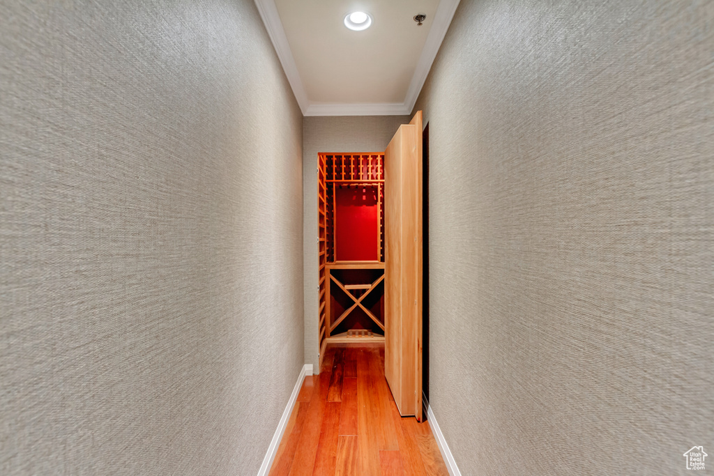 Corridor with light wood-type flooring, ornamental molding, recessed lighting, and a textured wall