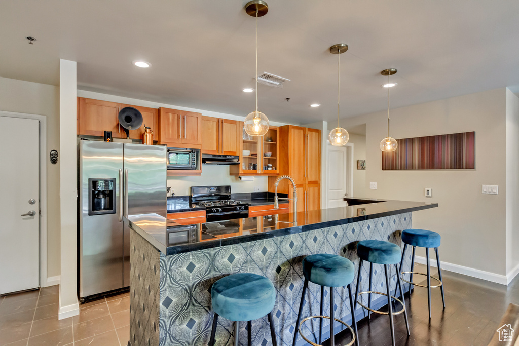 Kitchen with stainless steel appliances, dark countertops, a kitchen breakfast bar, recessed lighting, and a center island with sink