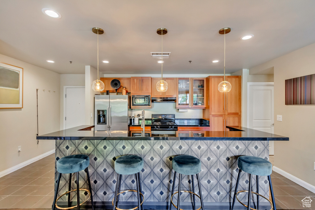 Kitchen featuring dark countertops, dark tile patterned flooring, appliances with stainless steel finishes, a kitchen bar, and recessed lighting