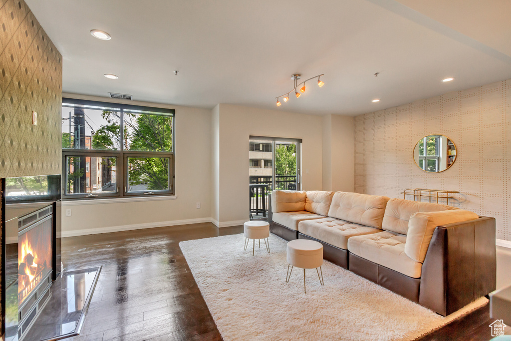 Living room featuring dark wood finished floors, recessed lighting, wallpapered walls, an accent wall, and a lit fireplace