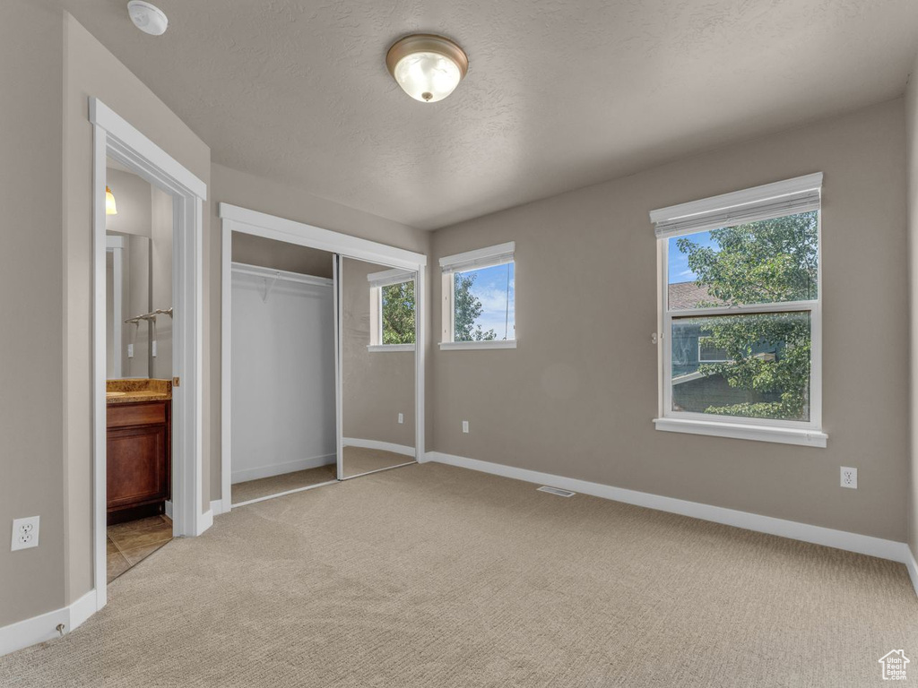 Unfurnished bedroom with carpet, a closet, ensuite bathroom, and a textured ceiling