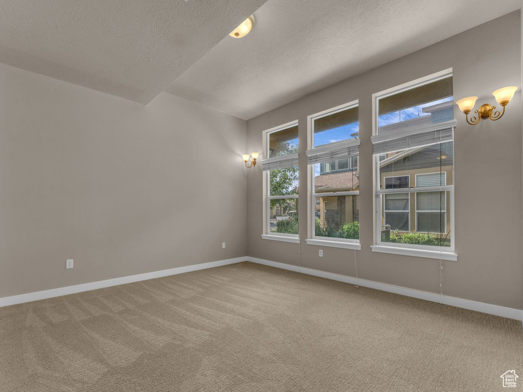 Empty room with carpet flooring, a textured ceiling, and a chandelier