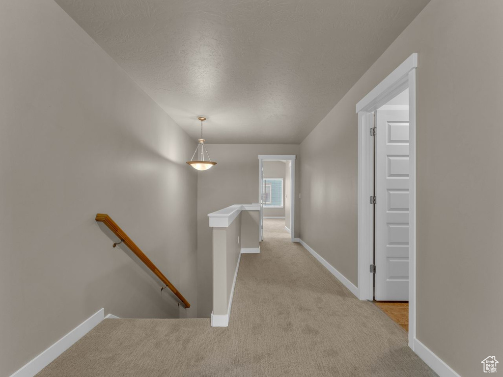 Hallway featuring an upstairs landing, carpet floors, and a textured ceiling