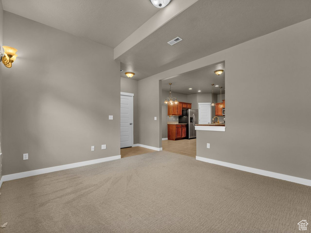 Unfurnished living room featuring light carpet and a chandelier