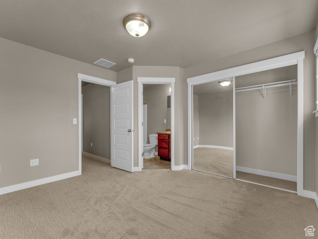 Unfurnished bedroom with a closet, carpet floors, and connected bathroom