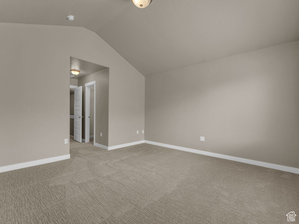 Carpeted spare room featuring vaulted ceiling and baseboards
