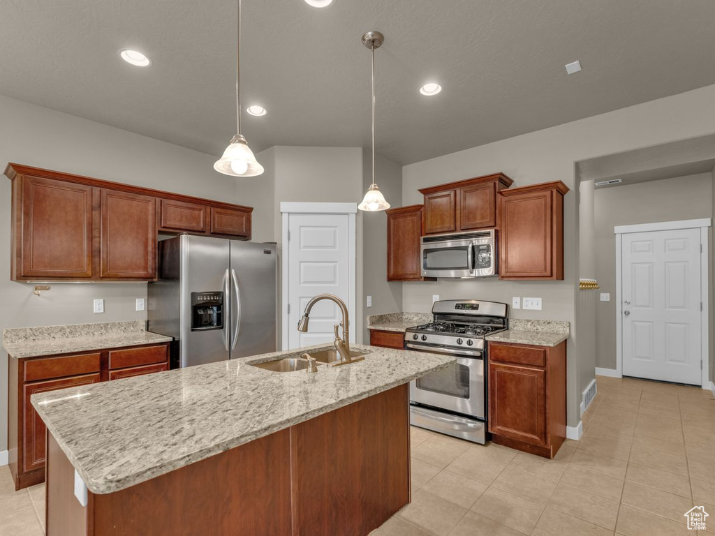 Kitchen featuring stainless steel appliances, an island with sink, light stone counters, decorative light fixtures, and light tile patterned flooring