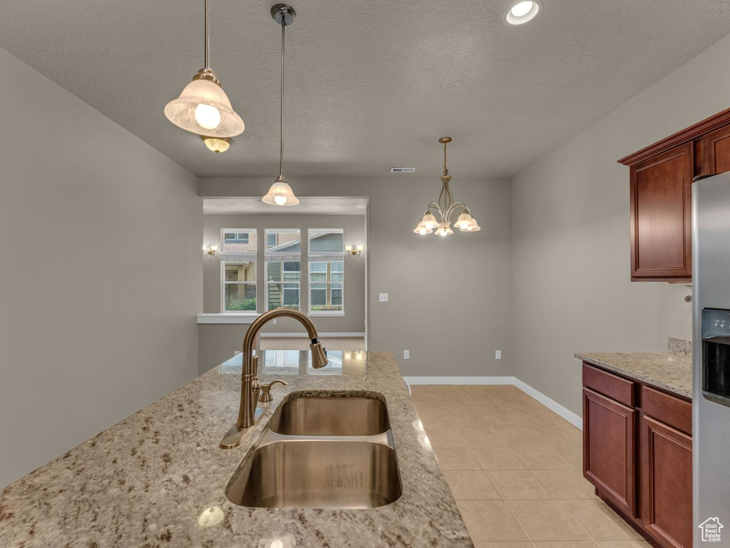 Kitchen with stainless steel fridge with ice dispenser, hanging light fixtures, light stone countertops, and light tile patterned flooring