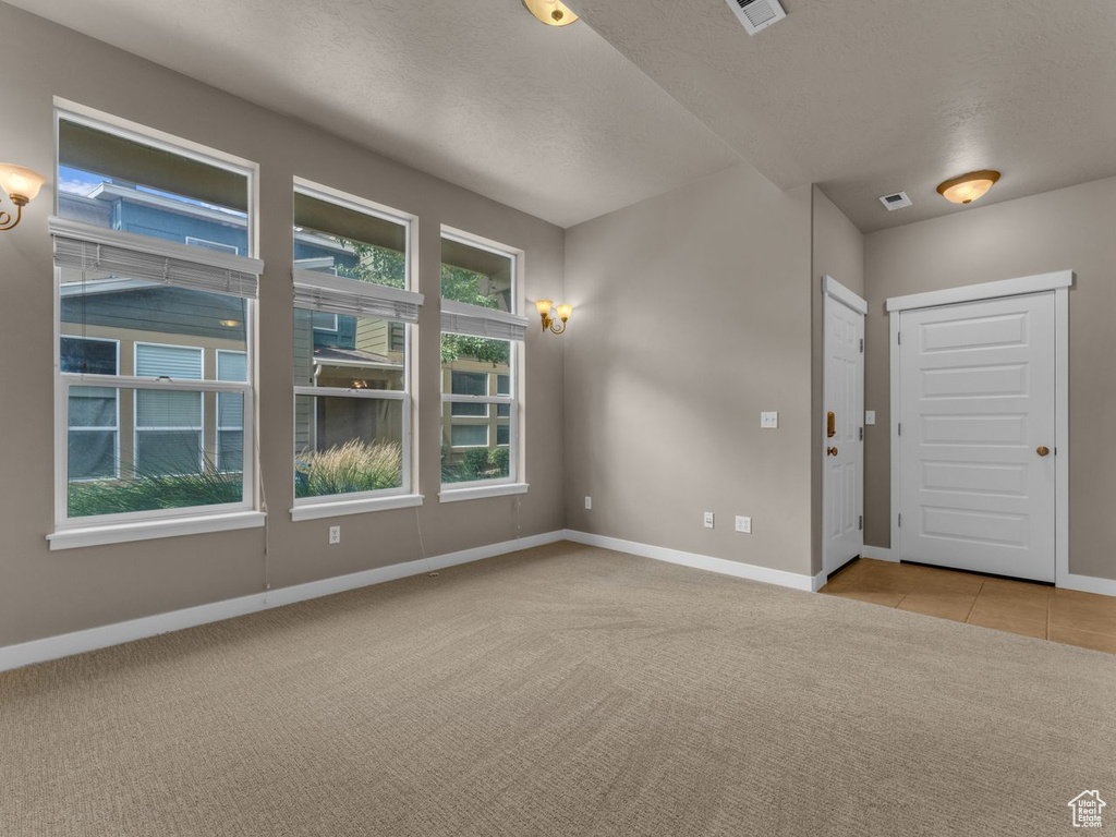 Carpeted empty room with a textured ceiling and tile patterned flooring