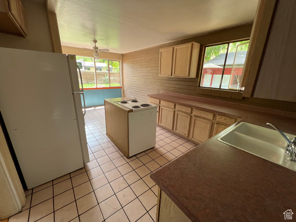 Kitchen featuring white appliances, light brown cabinetry, light tile patterned floors, and plenty of natural light