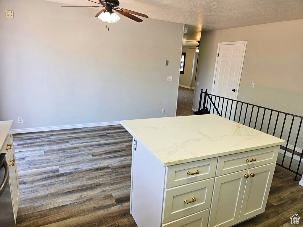Kitchen featuring ceiling fan, a kitchen island, dark wood finished floors, light stone countertops, and a textured ceiling
