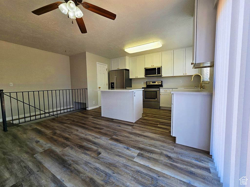Kitchen with a kitchen island, appliances with stainless steel finishes, dark wood-style floors, white cabinets, and a ceiling fan