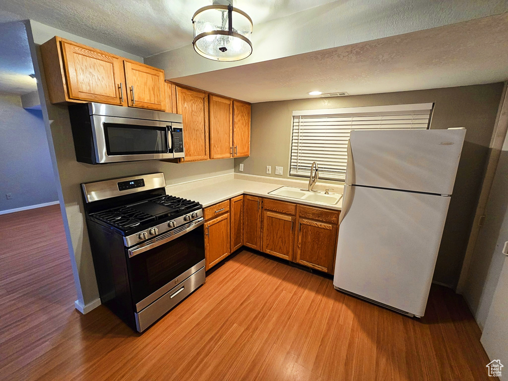 Kitchen with stainless steel appliances, light wood-style floors, light countertops, brown cabinetry, and a textured ceiling