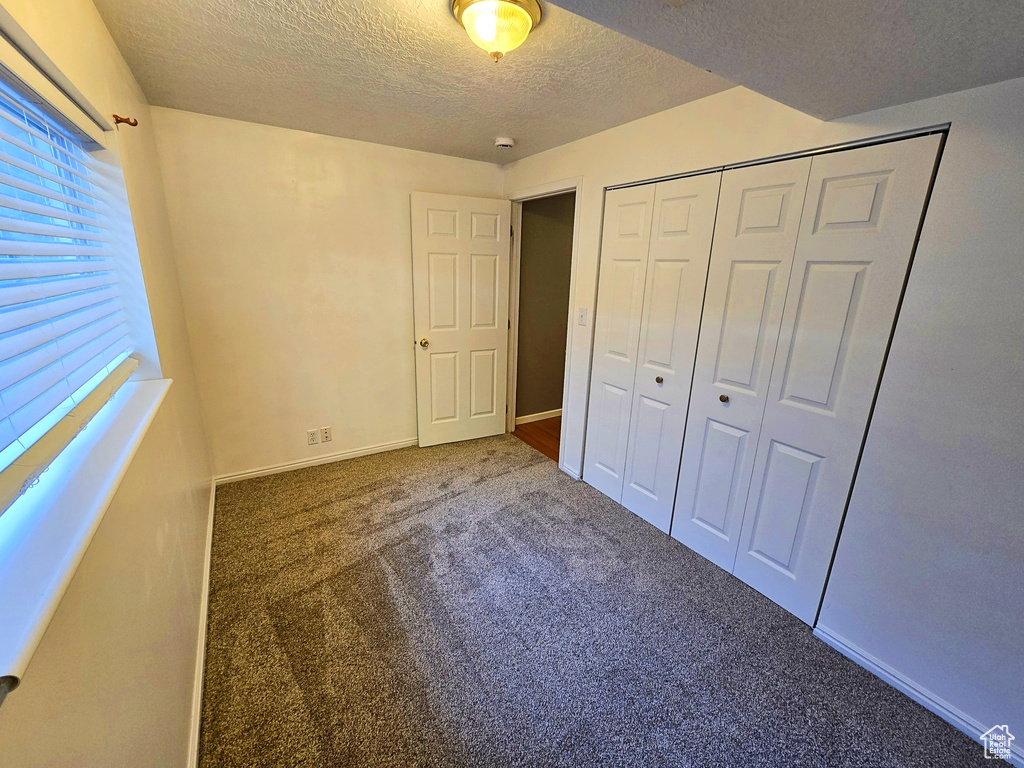 Unfurnished bedroom featuring a textured ceiling, carpet flooring, and a closet