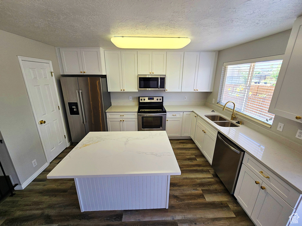 Kitchen with dark wood-type flooring, stainless steel appliances, a textured ceiling, a center island, and white cabinetry