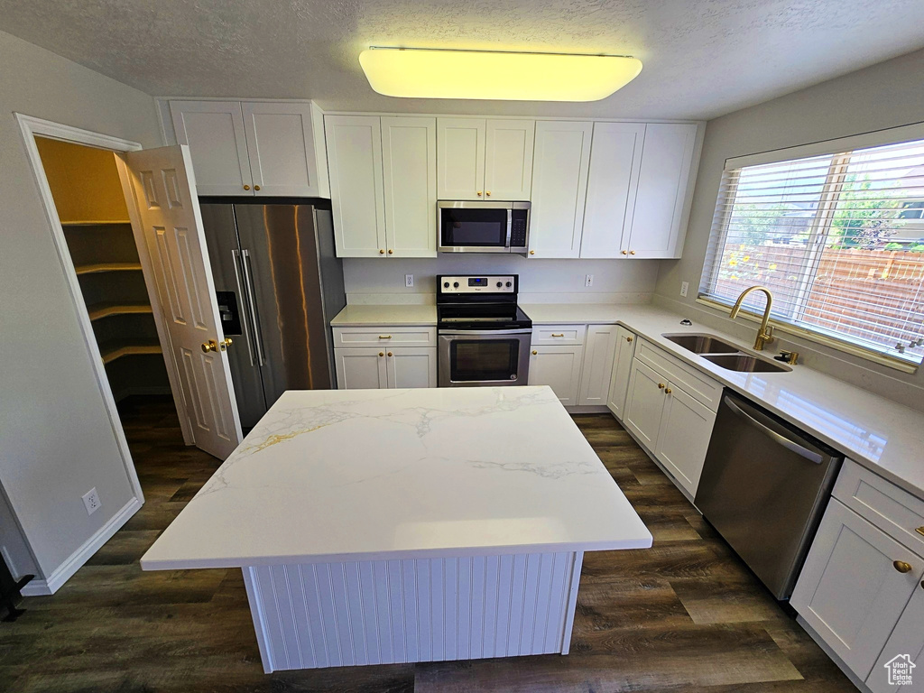 Kitchen featuring stainless steel appliances, a center island, dark wood finished floors, a textured ceiling, and white cabinets