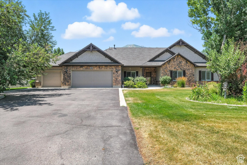 Craftsman inspired home with an attached garage, asphalt driveway, a front yard, stone siding, and stucco siding