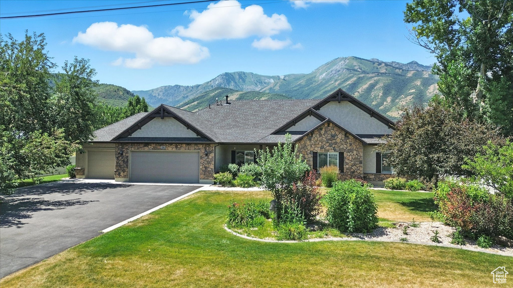 View of front facade with stone siding, an attached garage, asphalt driveway, a mountain view, and a front yard