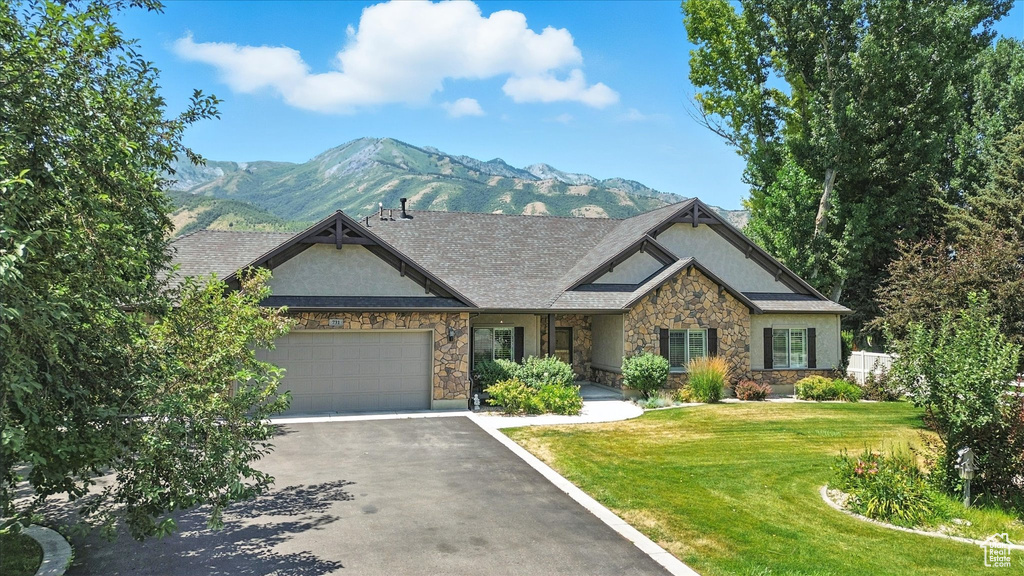View of front facade featuring a mountain view, an attached garage, stone siding, driveway, and a front lawn