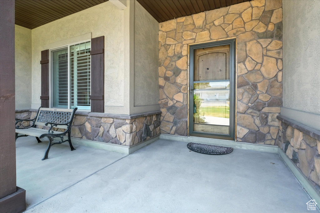 Doorway to property with stone siding, covered porch, and stucco siding
