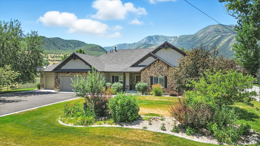 Craftsman house featuring stone siding, a mountain view, driveway, an attached garage, and a front yard