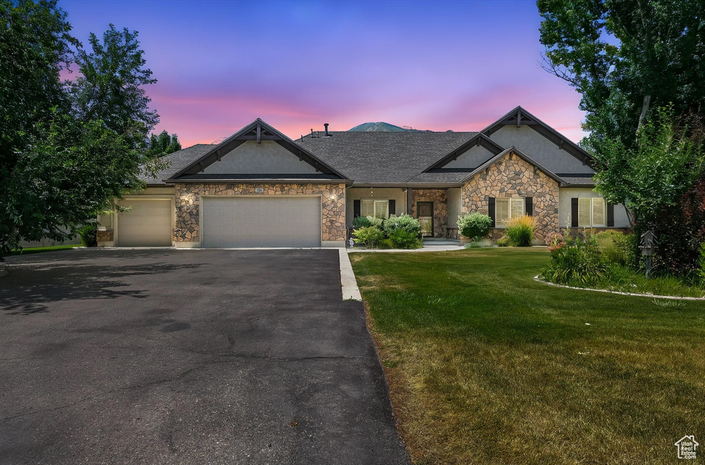 Craftsman-style home featuring asphalt driveway, an attached garage, a yard, and stone siding
