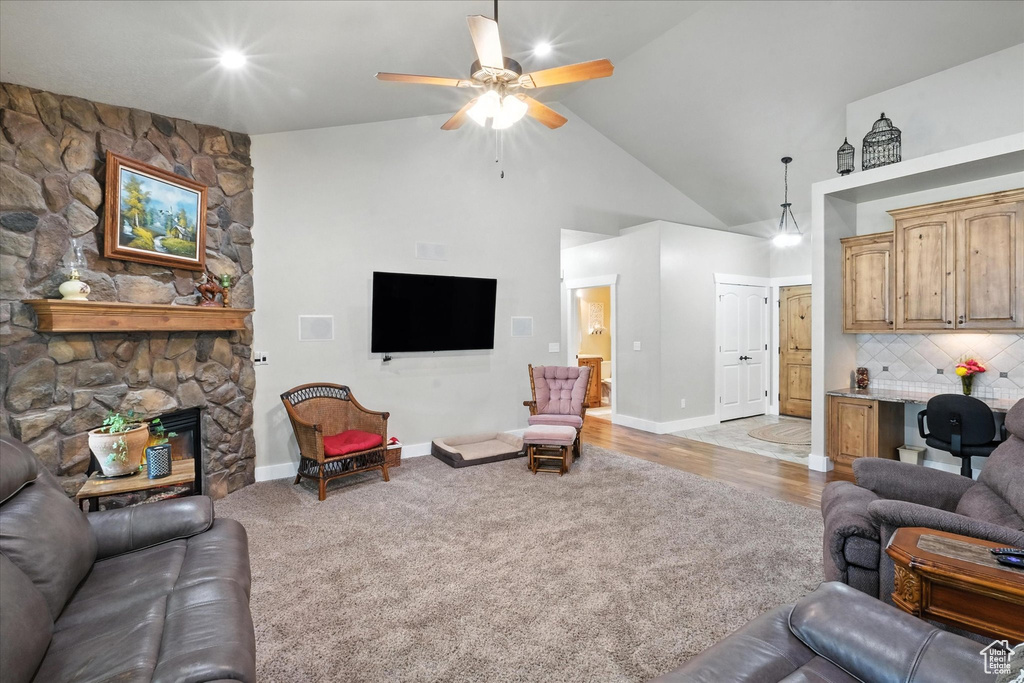 Living room with ceiling fan, light colored carpet, high vaulted ceiling, and a stone fireplace