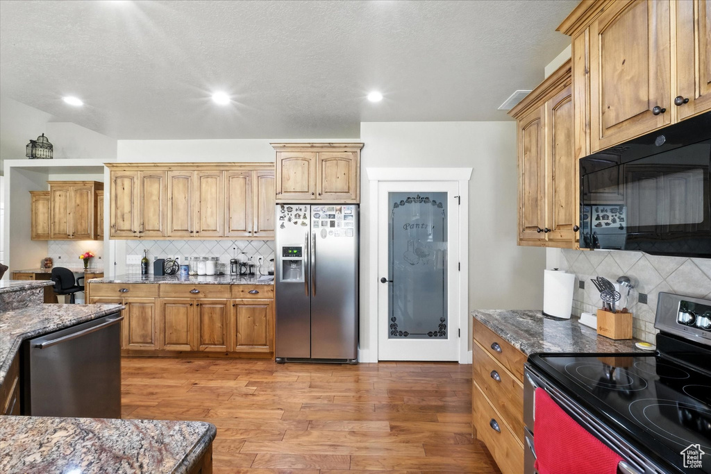 Kitchen featuring stainless steel appliances, backsplash, dark stone counters, recessed lighting, and a textured ceiling