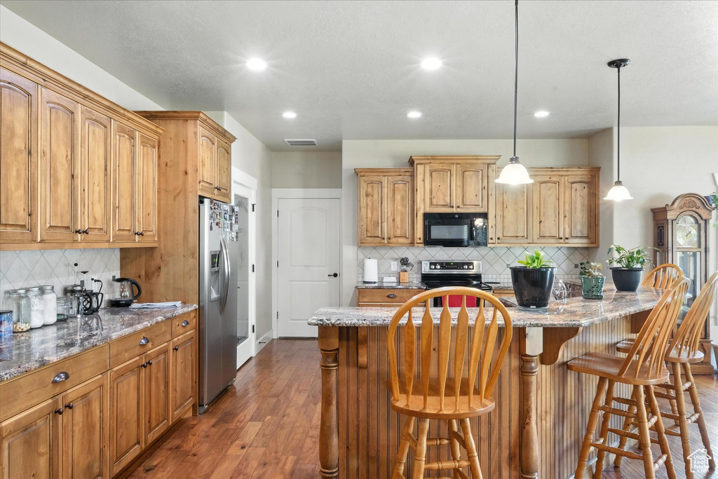 Kitchen featuring decorative backsplash, recessed lighting, light stone counters, dark wood-type flooring, and a kitchen breakfast bar