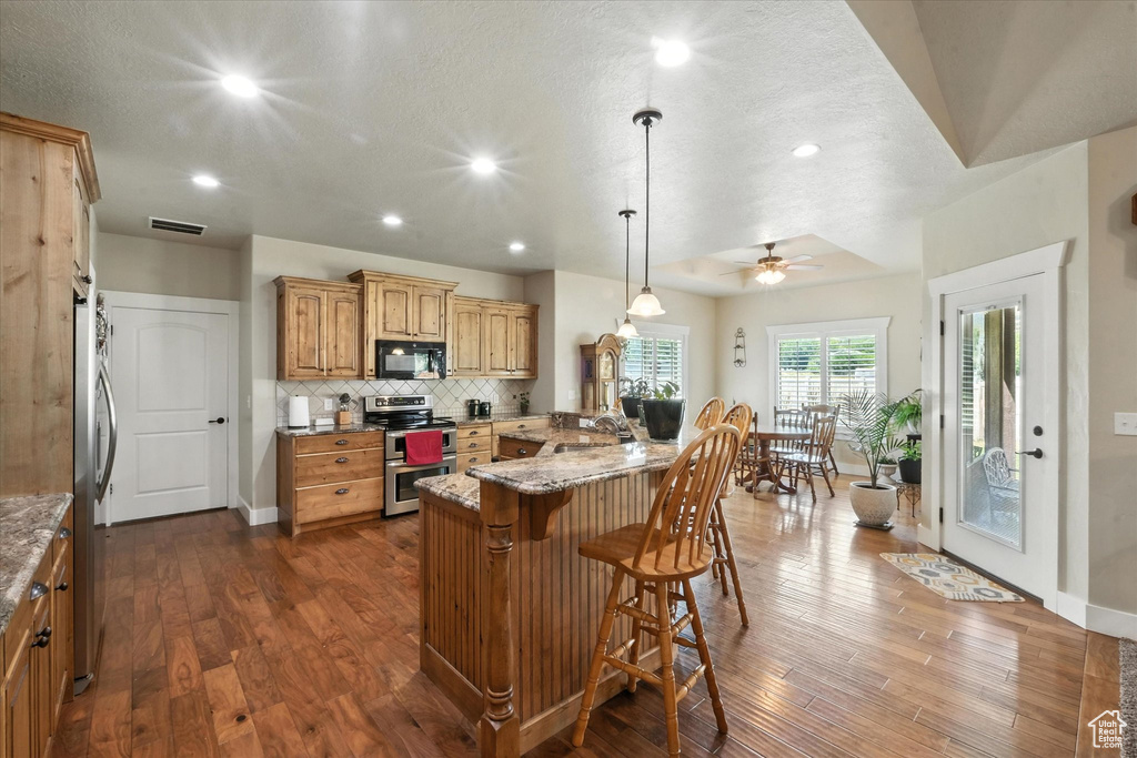 Kitchen featuring a breakfast bar, stainless steel appliances, dark wood finished floors, decorative backsplash, and recessed lighting