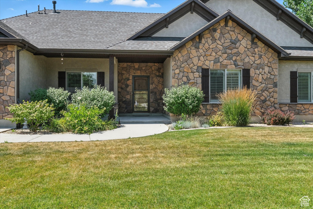 View of front of house featuring stone siding, stucco siding, a front lawn, and a shingled roof