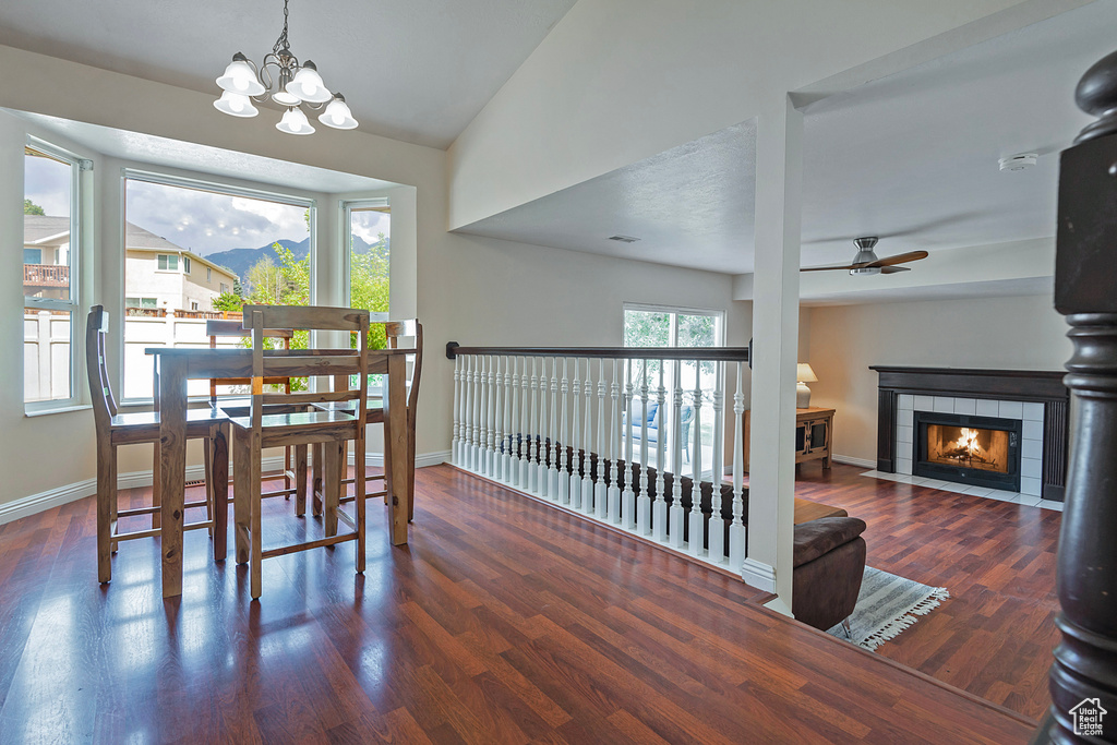Dining area featuring a ceiling fan, lofted ceiling, a chandelier, wood finished floors, and a fireplace