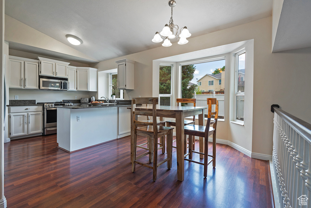 Kitchen featuring appliances with stainless steel finishes, dark wood finished floors, a chandelier, dark countertops, and lofted ceiling