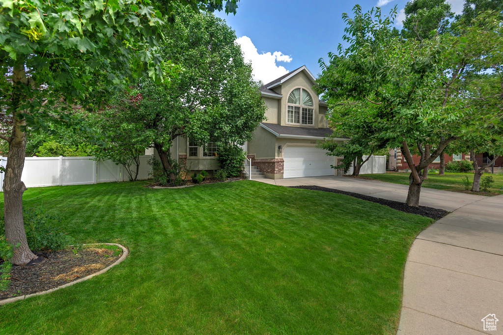 View of property hidden behind natural elements featuring stucco siding, brick siding, driveway, and an attached garage