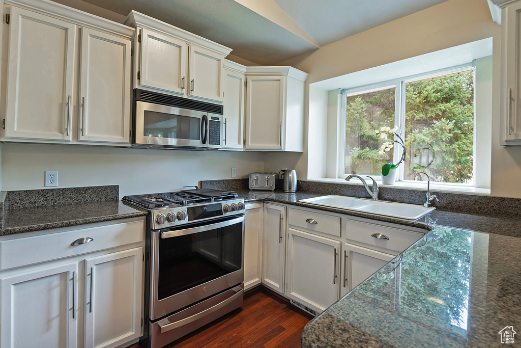 Kitchen featuring stainless steel appliances, vaulted ceiling, dark wood-style flooring, dark stone counters, and white cabinets