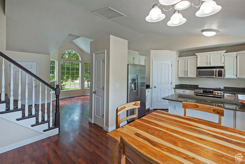 Kitchen with vaulted ceiling, stainless steel appliances, white cabinetry, dark wood-style floors, and a peninsula