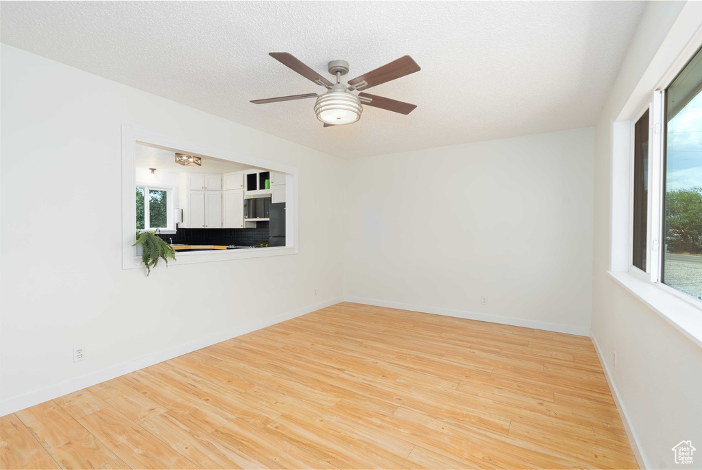 Spare room with plenty of natural light, wood finished floors, a ceiling fan, and a textured ceiling