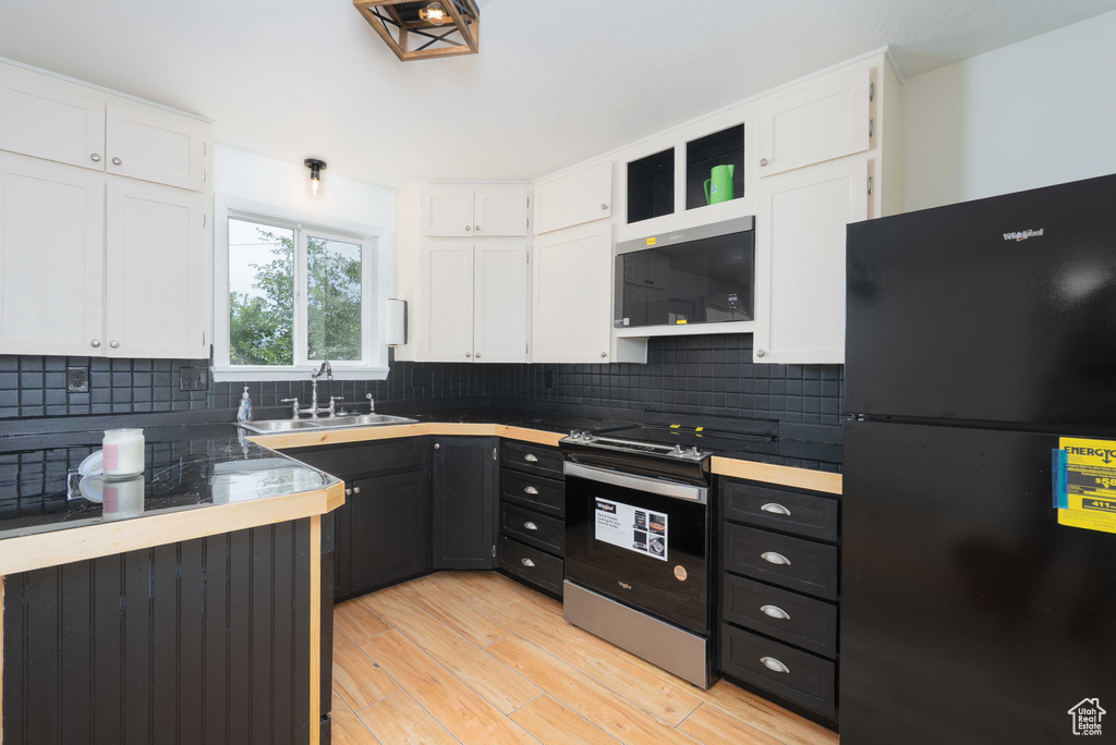 Kitchen with freestanding refrigerator, white cabinets, electric stove, and decorative backsplash