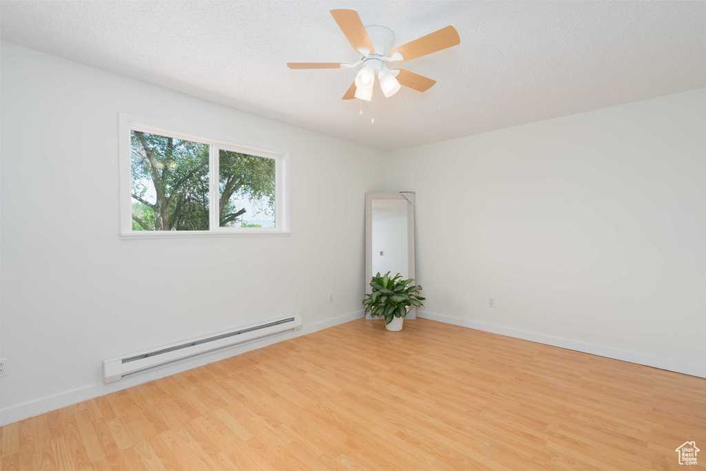 Unfurnished room featuring a baseboard heating unit, wood finished floors, and ceiling fan
