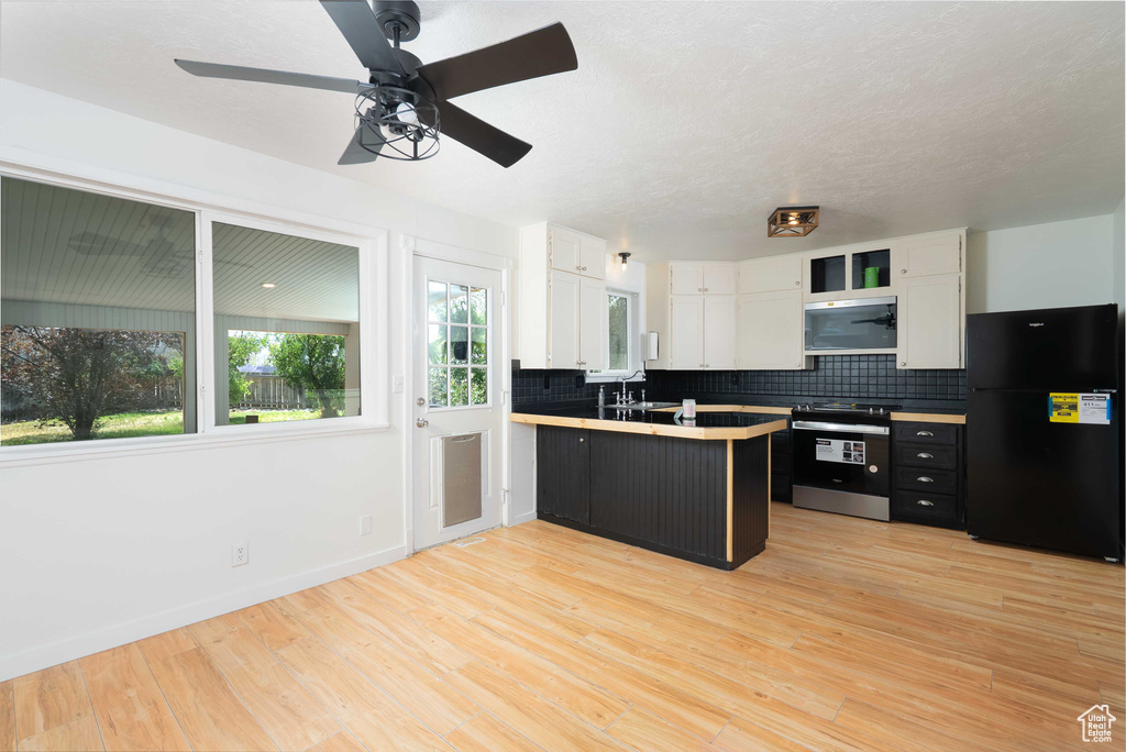 Kitchen featuring freestanding refrigerator, white cabinets, electric range, decorative backsplash, and a peninsula