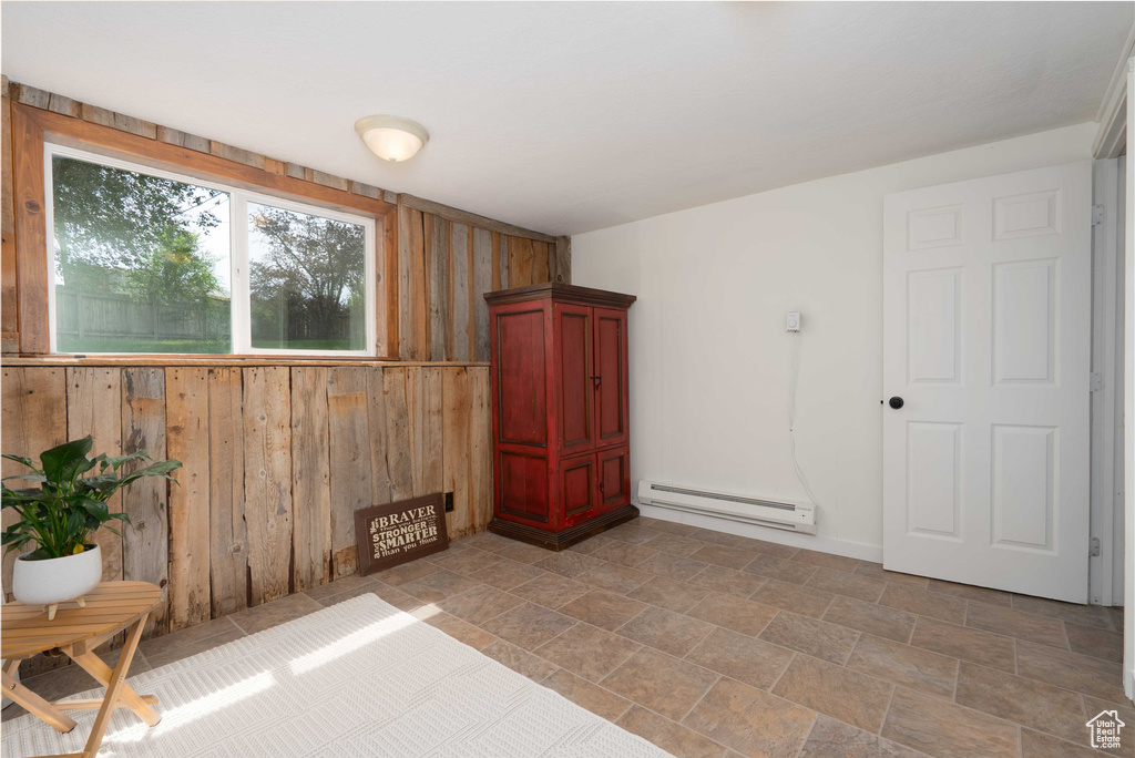 Unfurnished room with wood walls, baseboard heating, and light stone finish floors