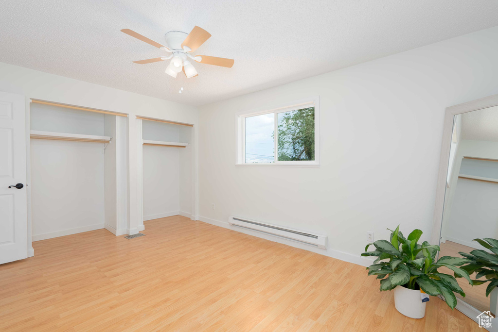 Unfurnished bedroom with a baseboard heating unit, light wood-style floors, two closets, and a ceiling fan